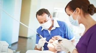 Ein Zahnarzt und seine Assistentin behandeln eine Patientin.
