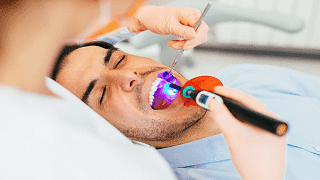 Auf einem Behandlungsstuhl härtet eine Zahnärztin die Zahnfüllung eines Patienten mit UV-Licht aus.